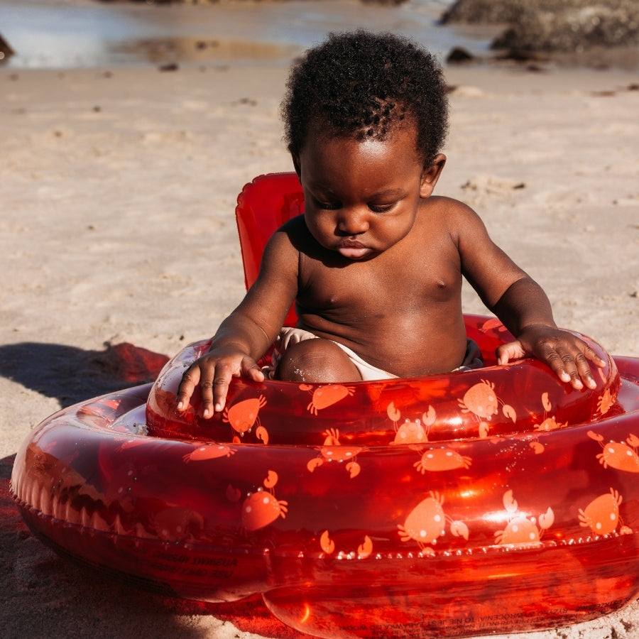 Child sitting in a transparant red baby float with crabs on it on a sandy beach