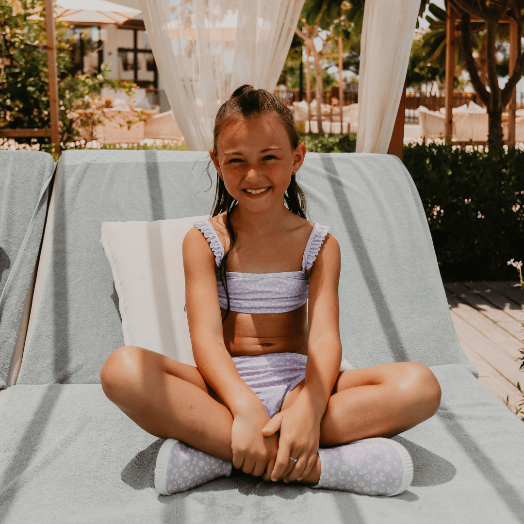 Young girl in a purple bikini sitting on a lounge chair outdoors.