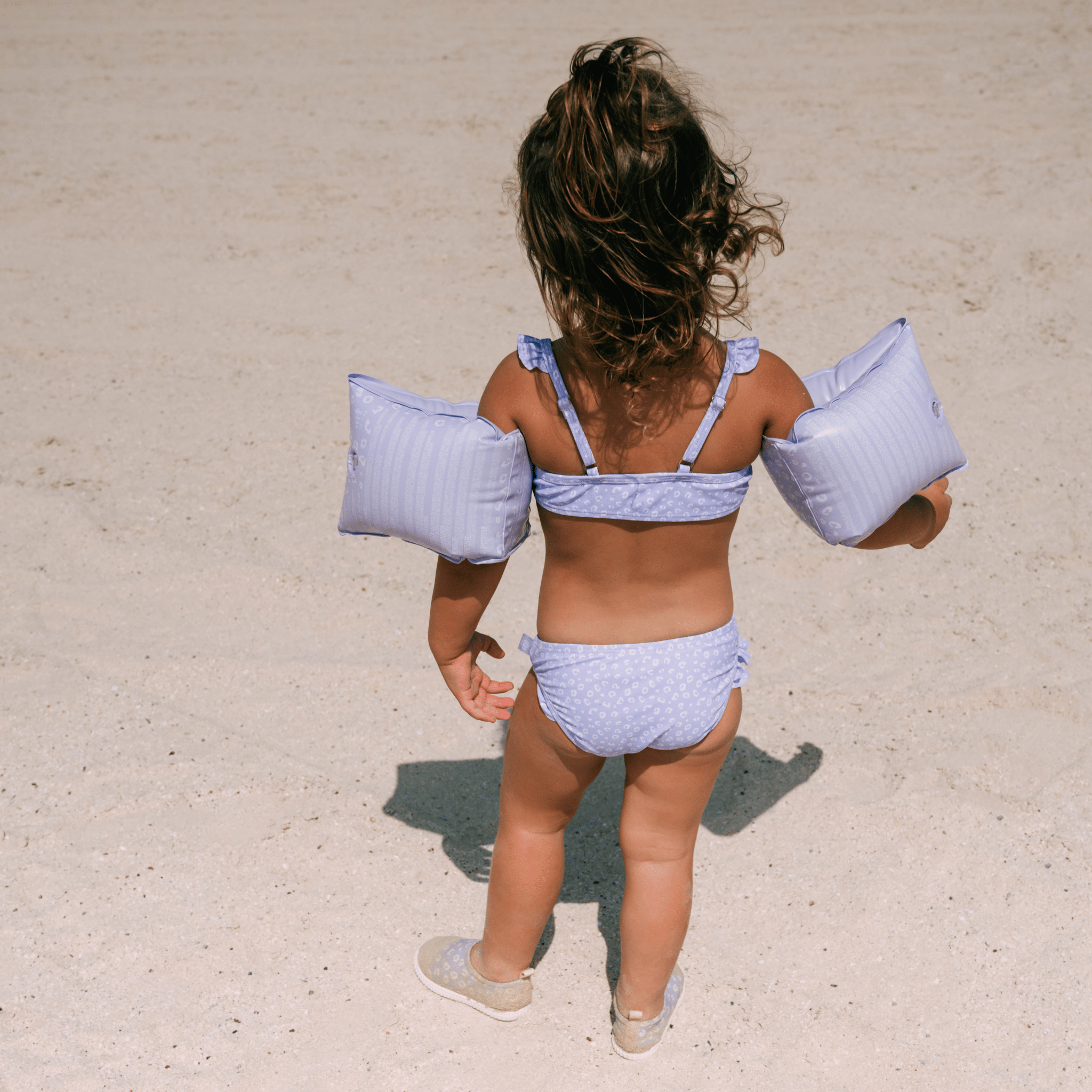 Child in a purple bikini with arm floats on a sandy beach