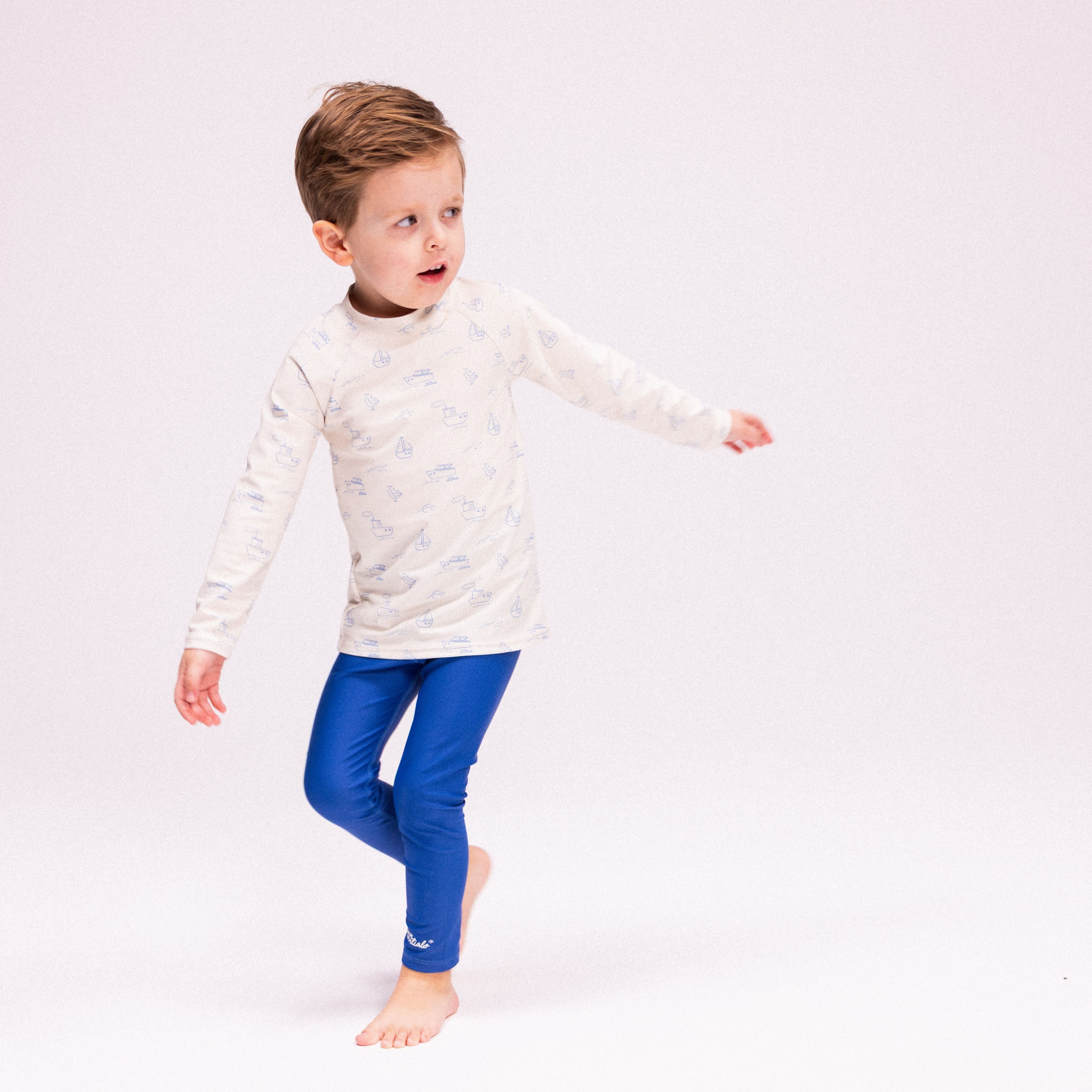 Child wearing a white long-sleeve shirt and blue leggings on a light gray background