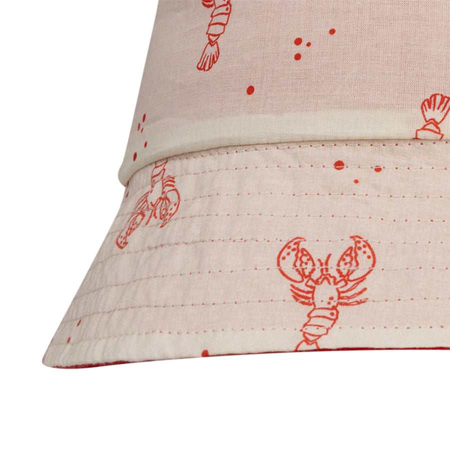 Close-up of a beige fabric sun hat with red lobster prints on a white background