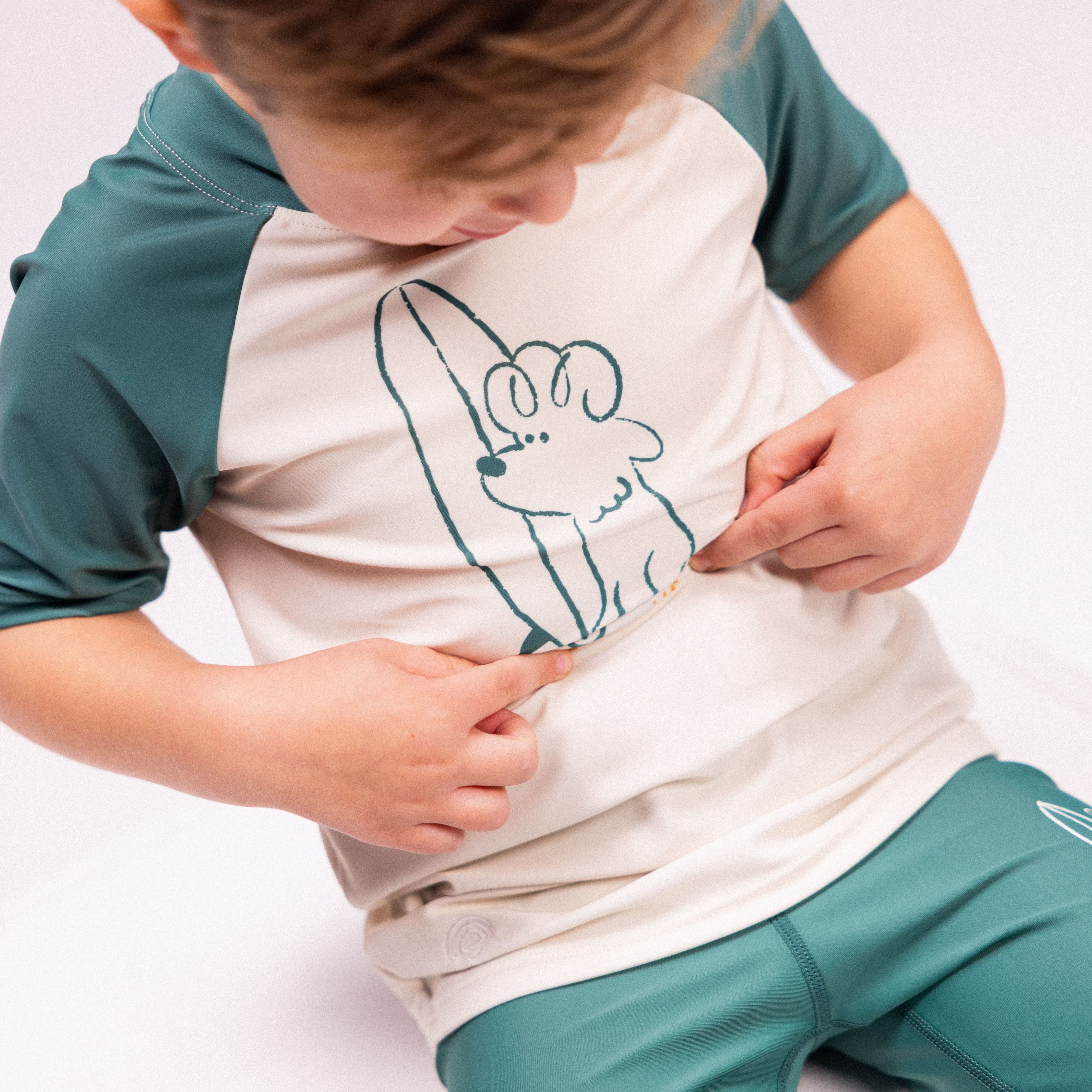 Child wearing a white and green shirt with a graphic design on a plain background