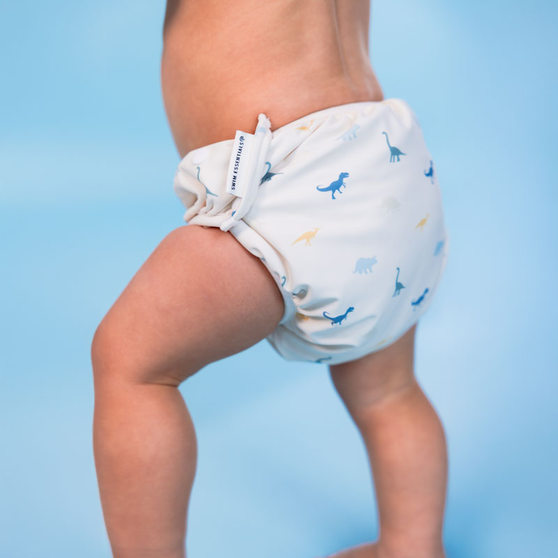 Baby wearing a white swim diaper with blue dinosaur prints against a light blue background