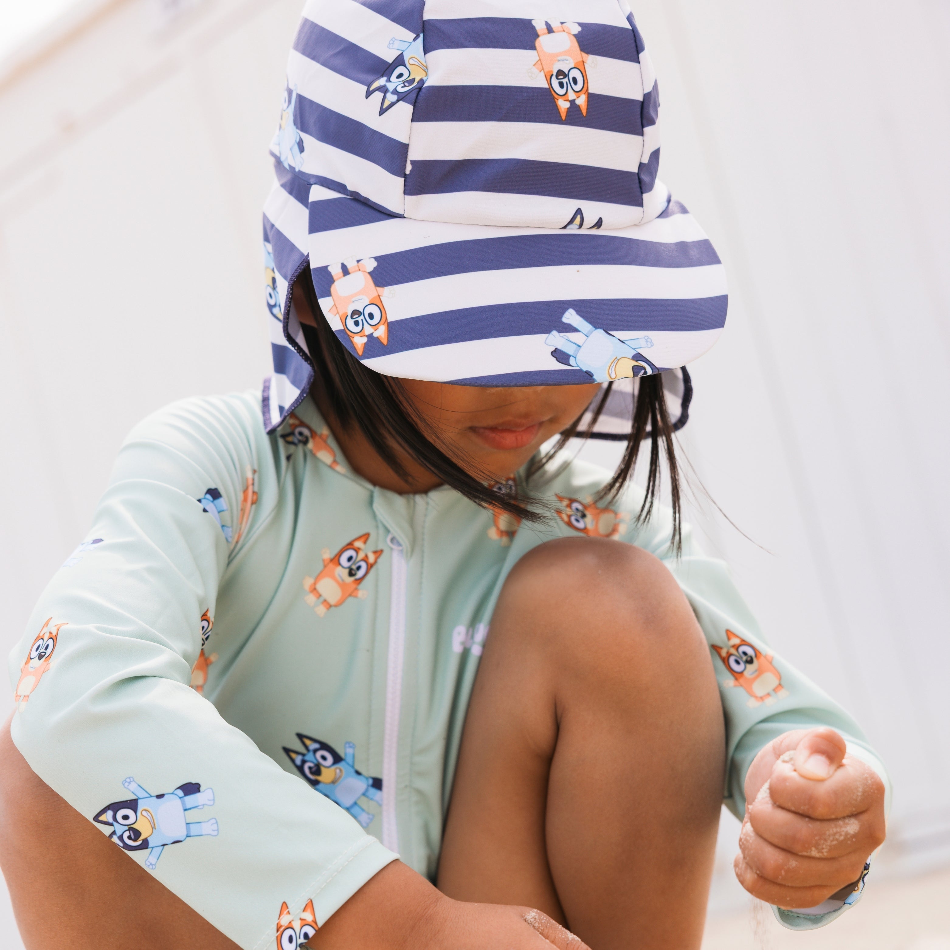 Child wearing a light green swimsuit with cartoon designs and a striped hat with animal prints.