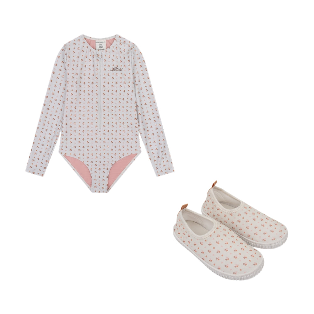 This is a set comprising a long-sleeved swimsuit and water shoes. The swimsuit has long sleeves, is old pink in colour and features a print of small hearts. The inside of the swimsuit is light pink. The Swim Essentials logo is also featured in the top right-hand corner. The water shoes are also old pink and feature the same print with small hearts. The sole of the shoes is white. They are shown against a white background.
