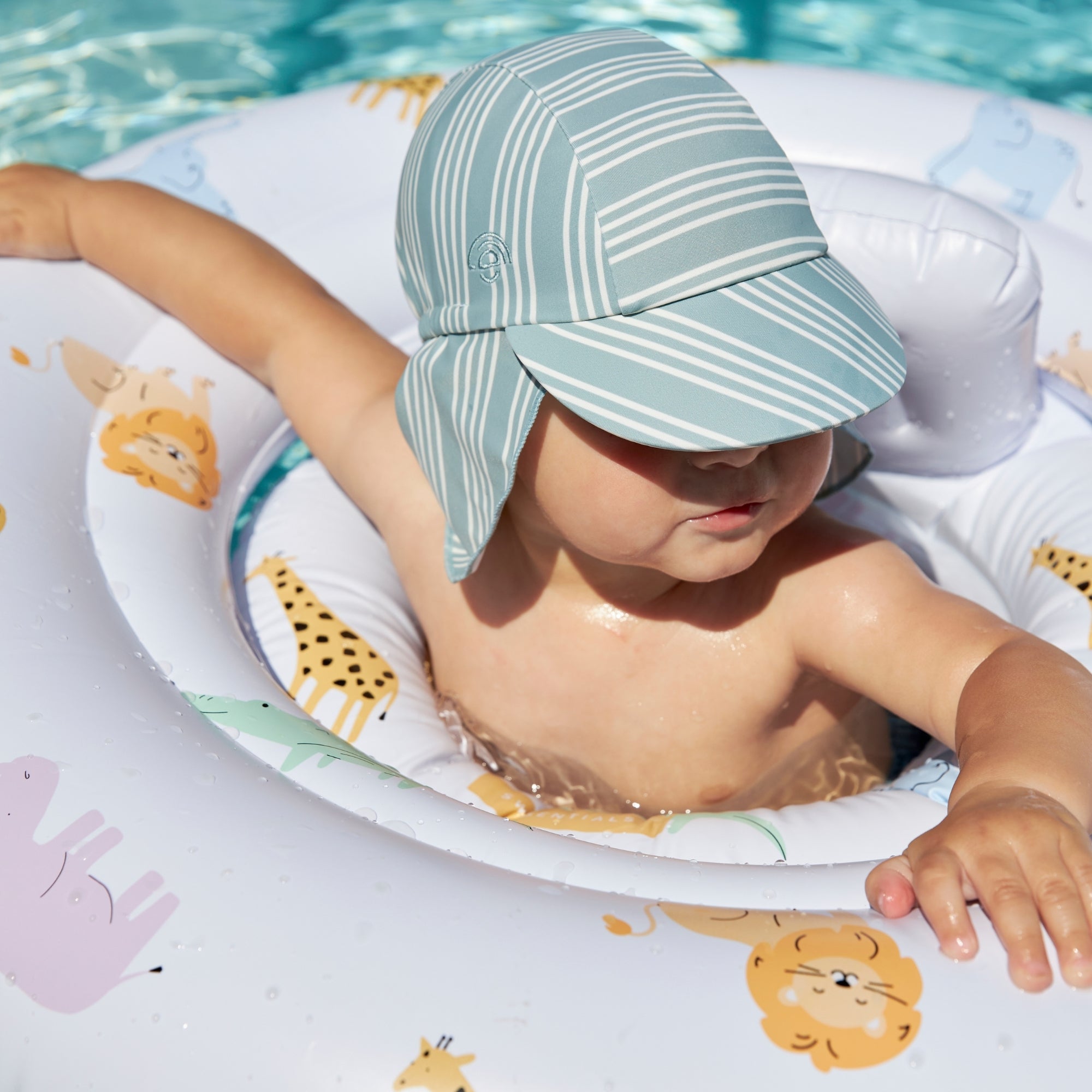 Child wearing a striped swim cap in a pool sitting in a white baby float with animal print on it.