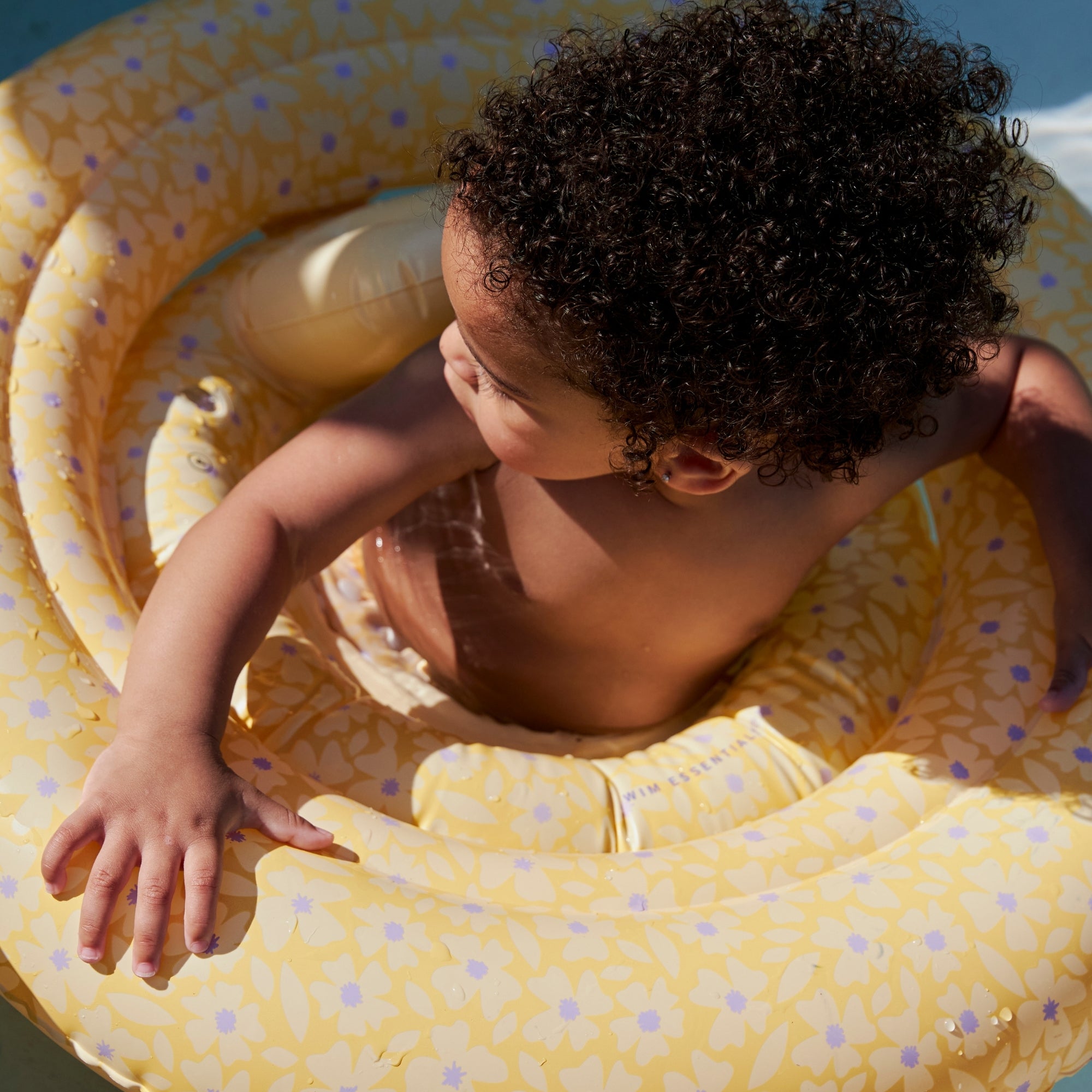 Small child in a yellow baby float with flowers with Purple polka dots on a sunny day.
