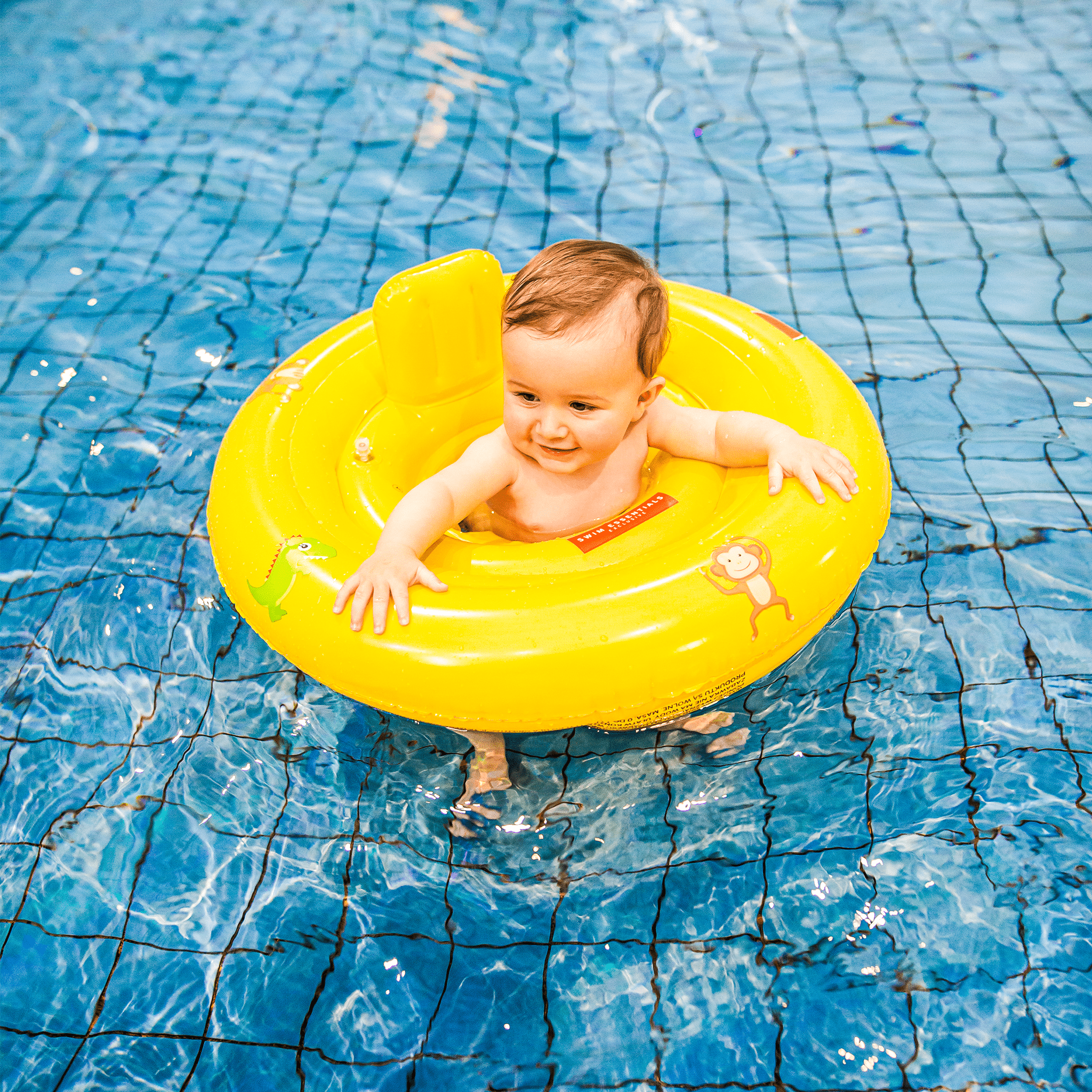 Baby in a yellow baby float with cartoons on it in a pool.