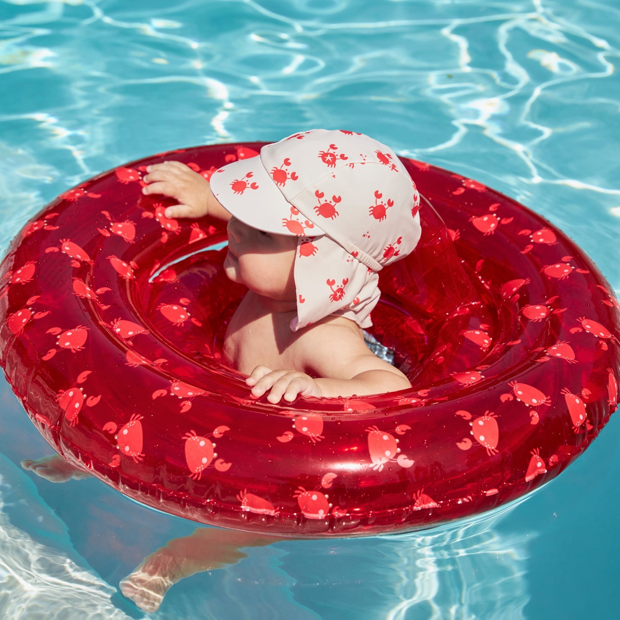Child in a red baby float with a crabby sun hat in clear blue water
