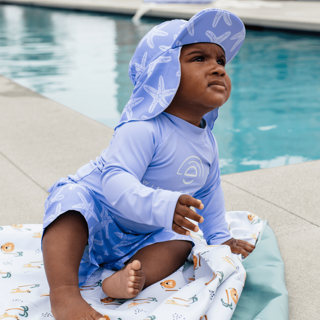 Baby with a purple outfit wearing a sun cap with UV protection sun cap, swimming T-Shirt and swim shorts