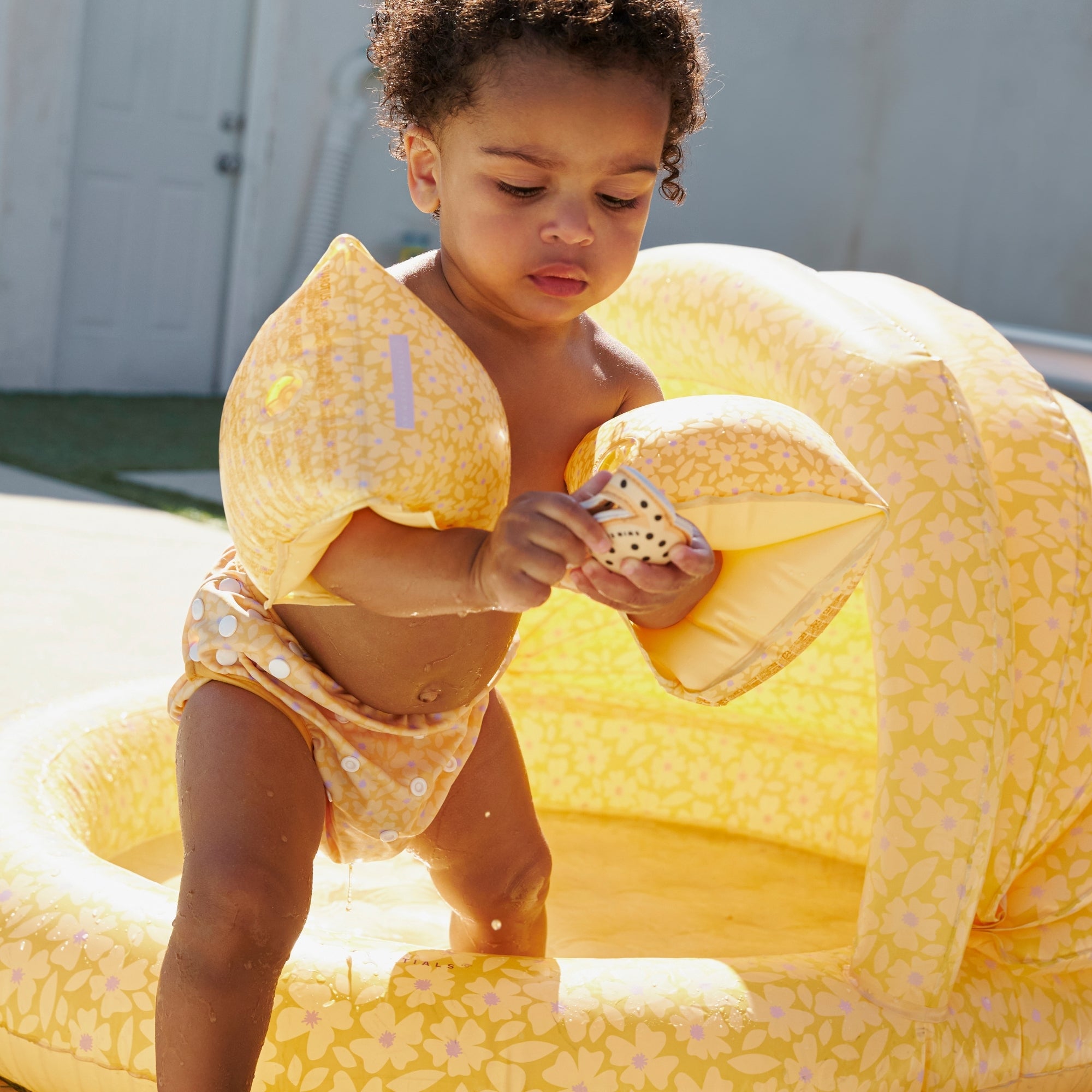 Child playing with a yellow inflatable pool toy outdoors