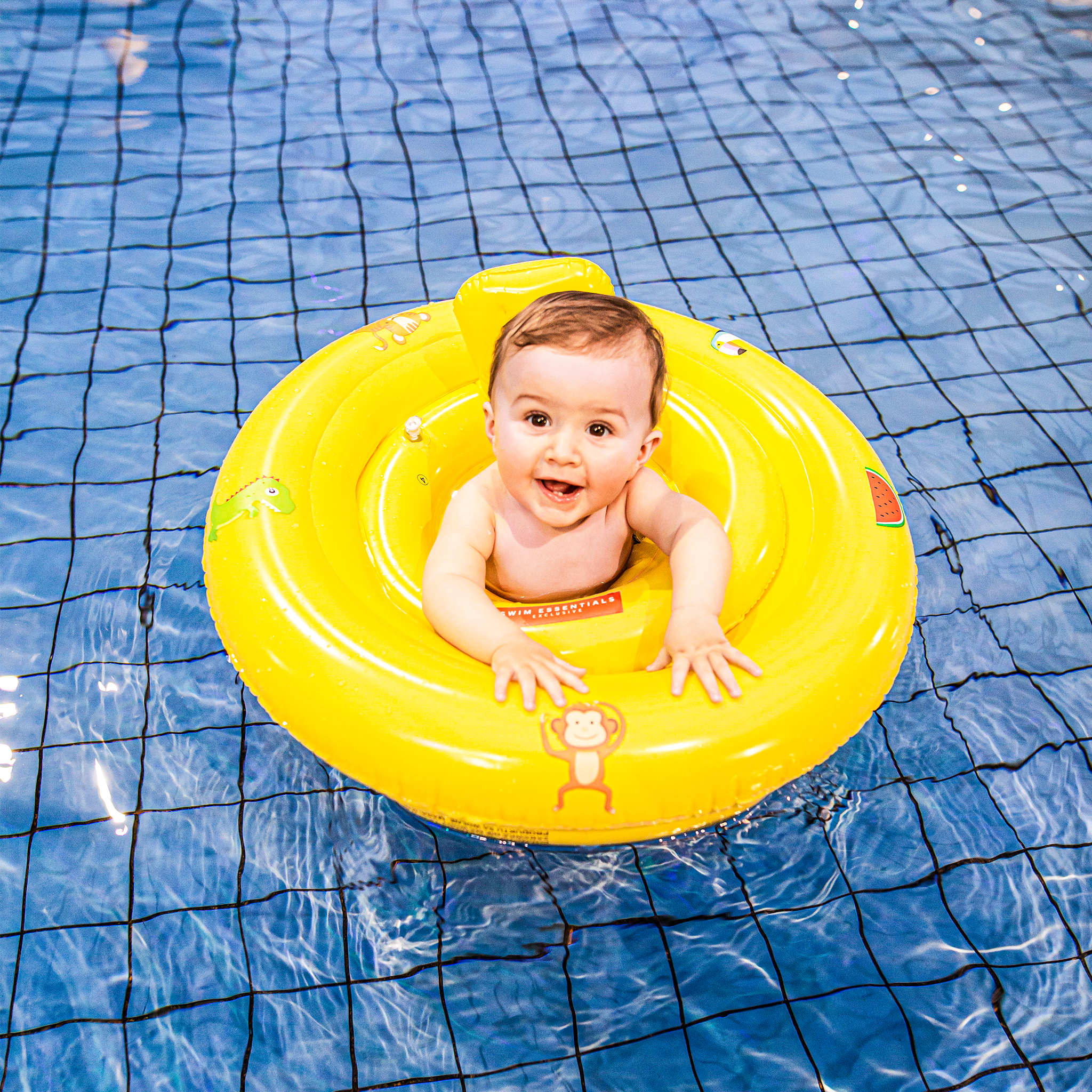 A happy baby in a yellow baby float with cartoons on it in a pool.