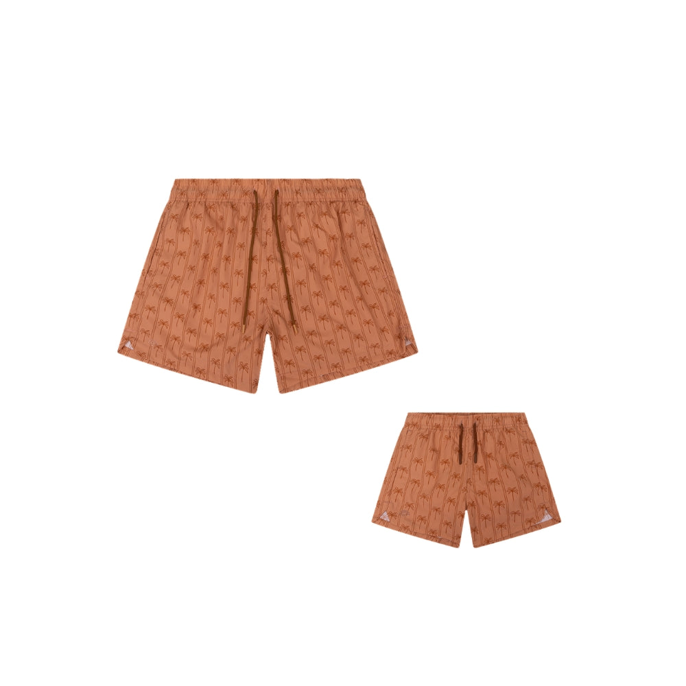This is a set comprising a pair of men’s swim shorts and a pair of boys’ swim shorts. The swim shorts are brown and feature stripes and palm trees. There is also a white background. 
