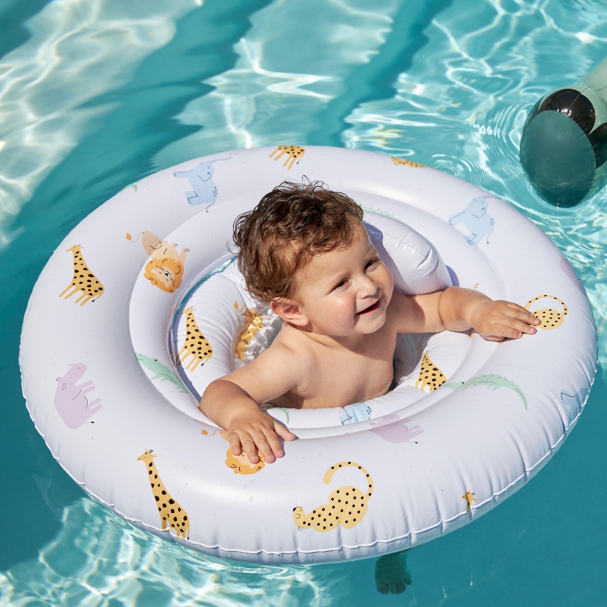 Happy small child who looks up in a white baby float with animal prints on it in clear blue water.
