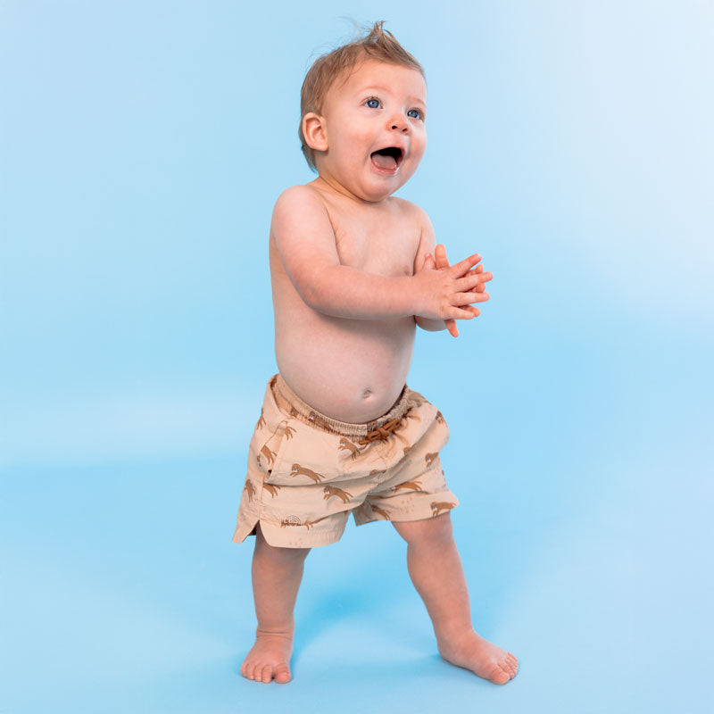 Baby wearing beige swim shorts with a pattern on a blue background