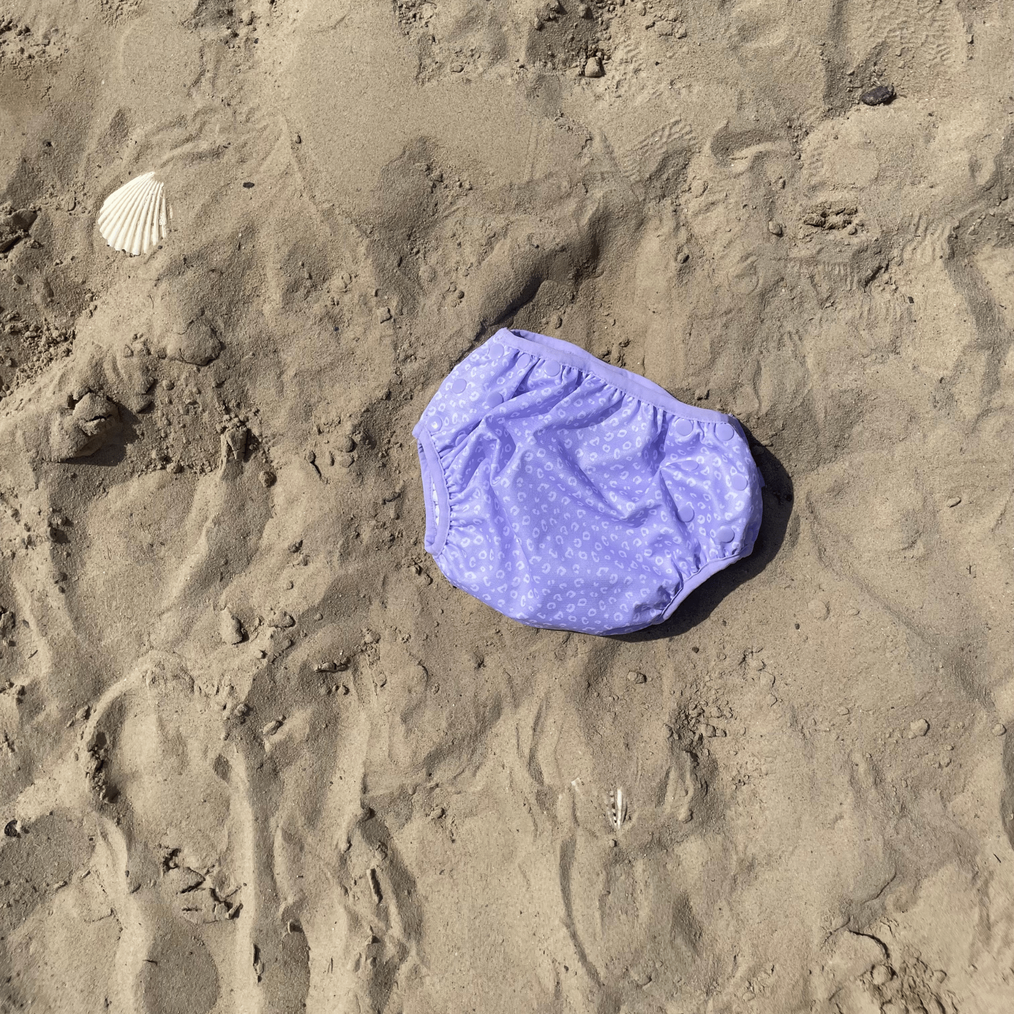 Purple swim diaper with white leopard pattern on sandy background