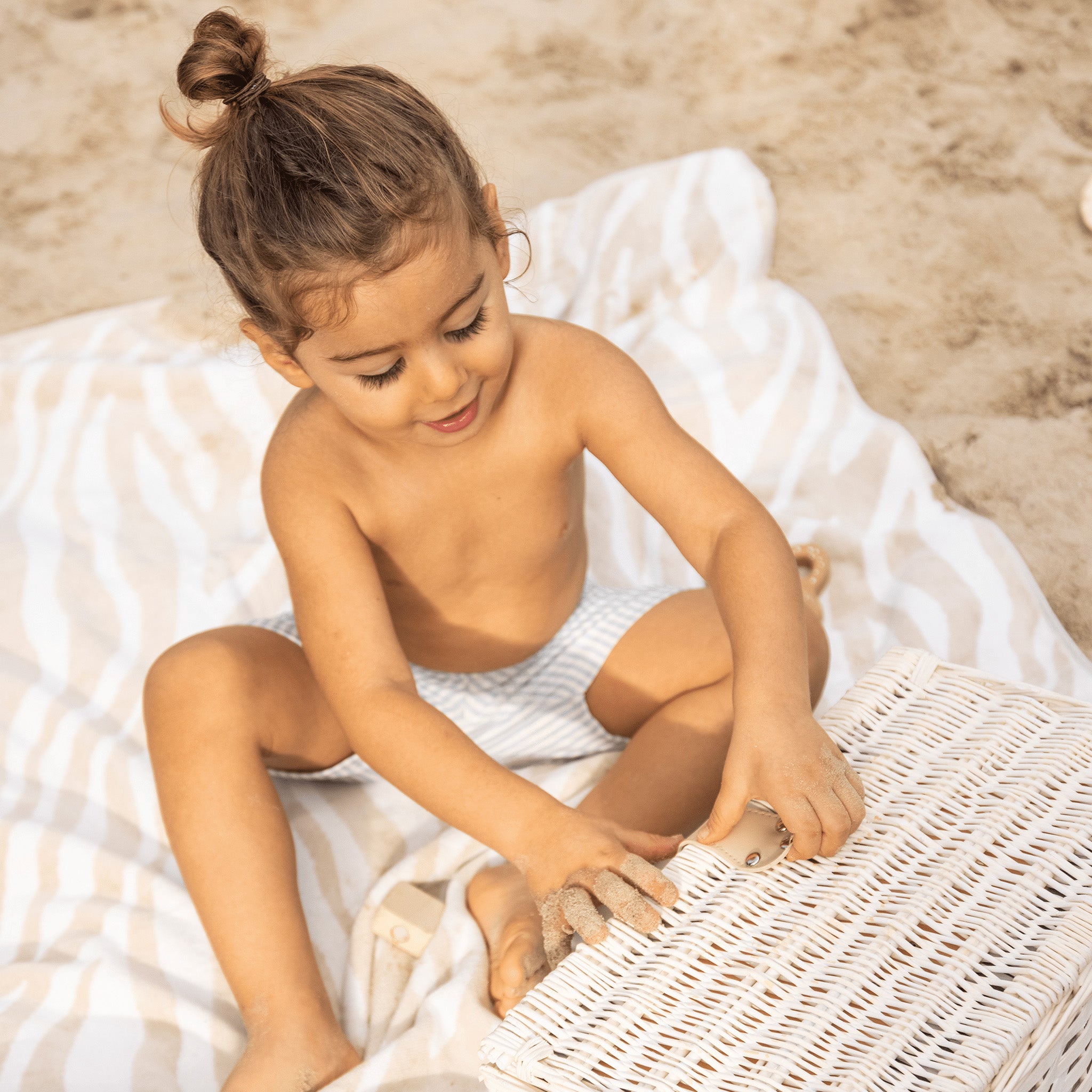 A child sitting on a towel at the beach wearing striped swim shorts