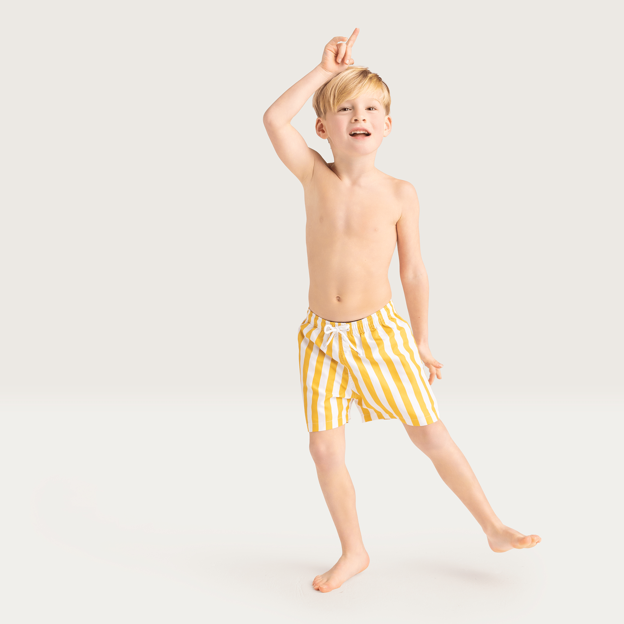 Young boy wearing yellow striped swim shorts on a white background