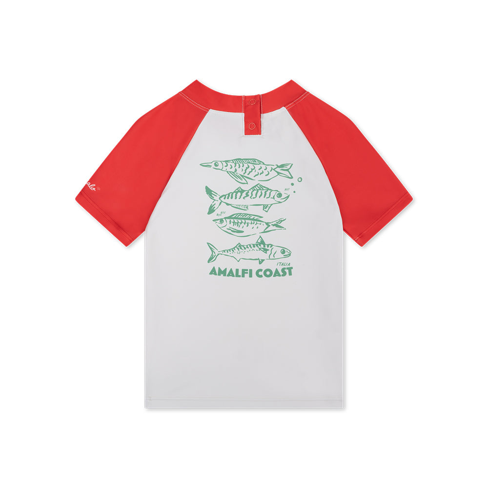 The back of a red-and-white short-sleeved swim shirt. The shirt is white and features green fish illustrations and the text “Amalfi Coast” The collar and short sleeves are red. On a white background. 
