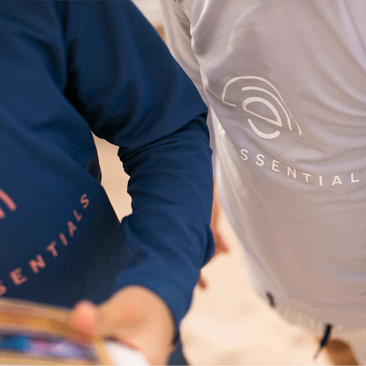 Two people wearing shirts with 'Swim Essentials' branding, one in blue with pink letters and the other in gray with white letters.