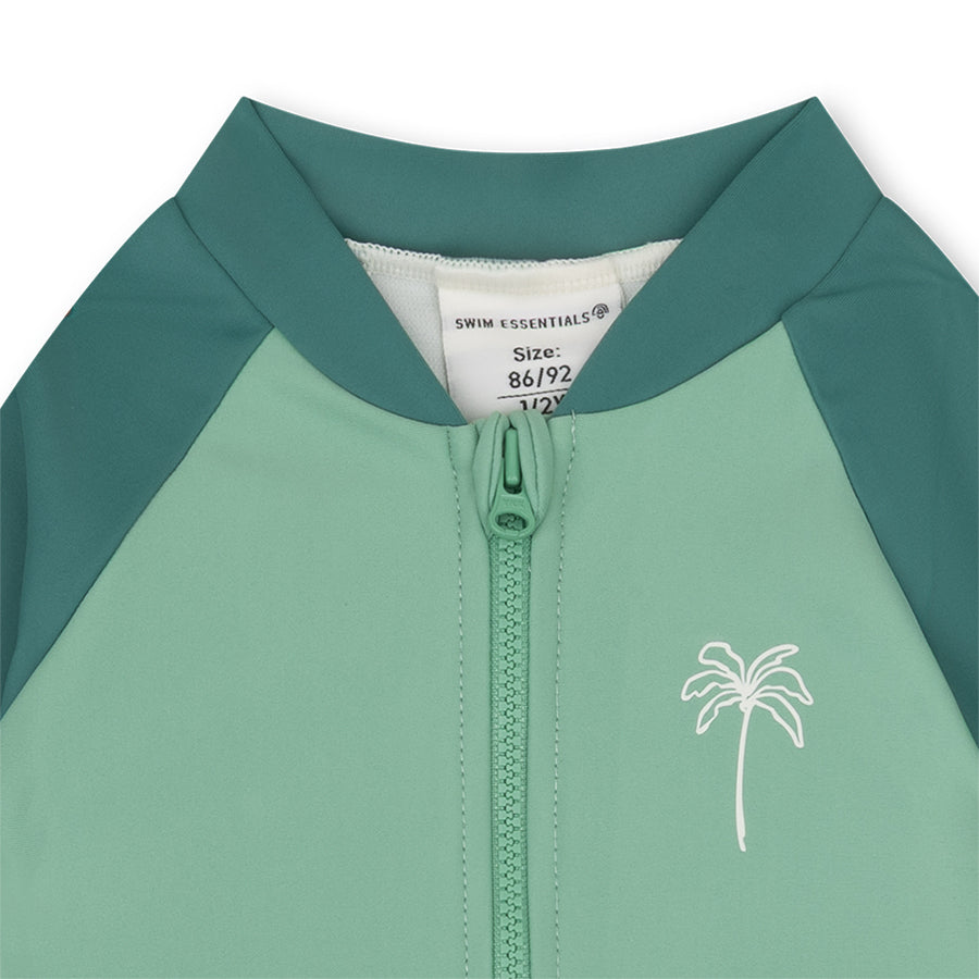 Close-up of a green and teal children's swimsuit with palm tree design and size label.