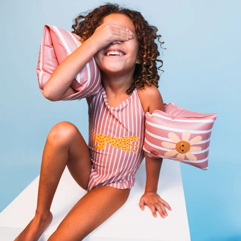 Child wearing a pink striped swimsuit with floral arm bands against a light blue background