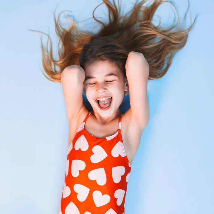 Child in a red swimsuit with white hearts lying on a blue background