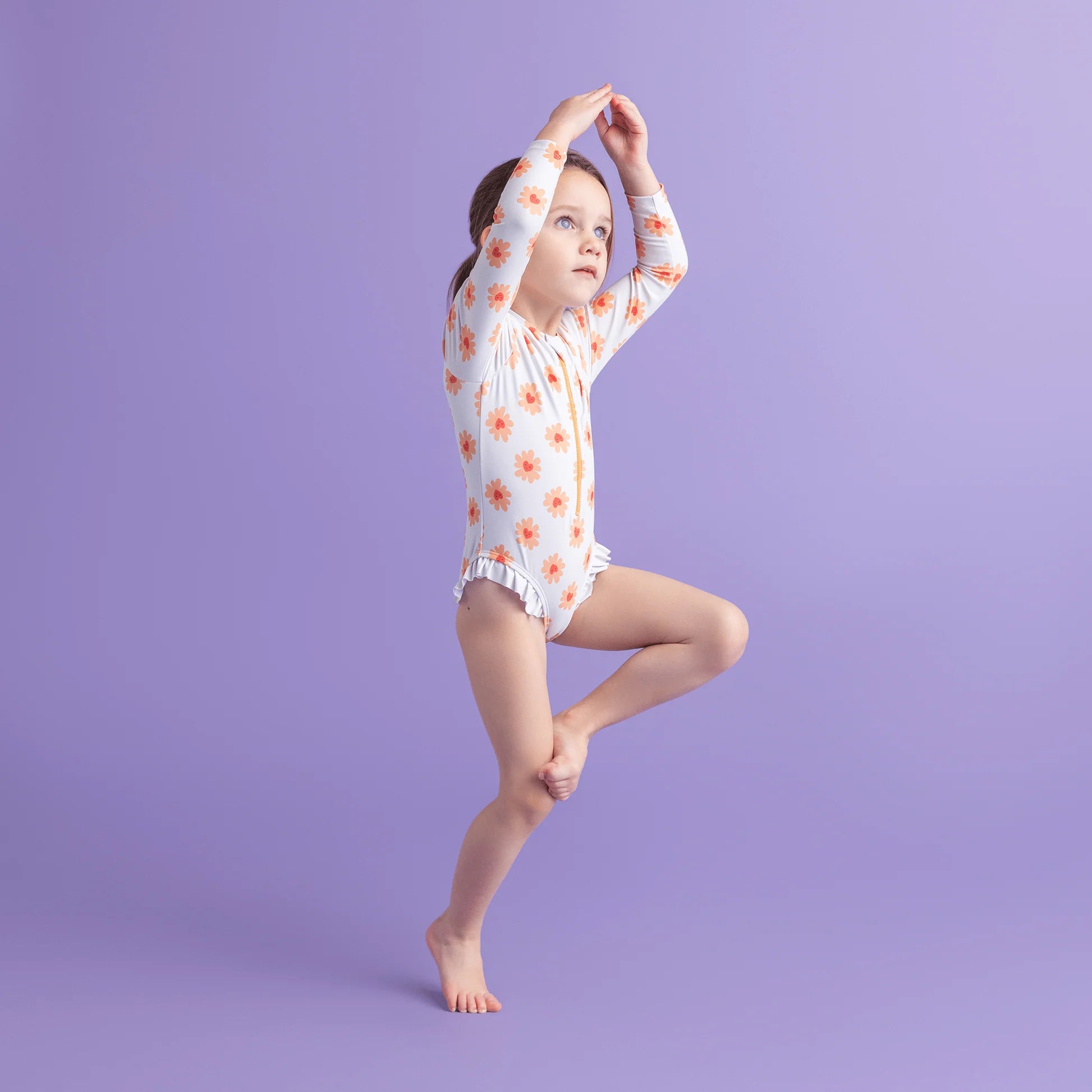 Young girl in a floral swimsuit with long sleeves posing against a purple background