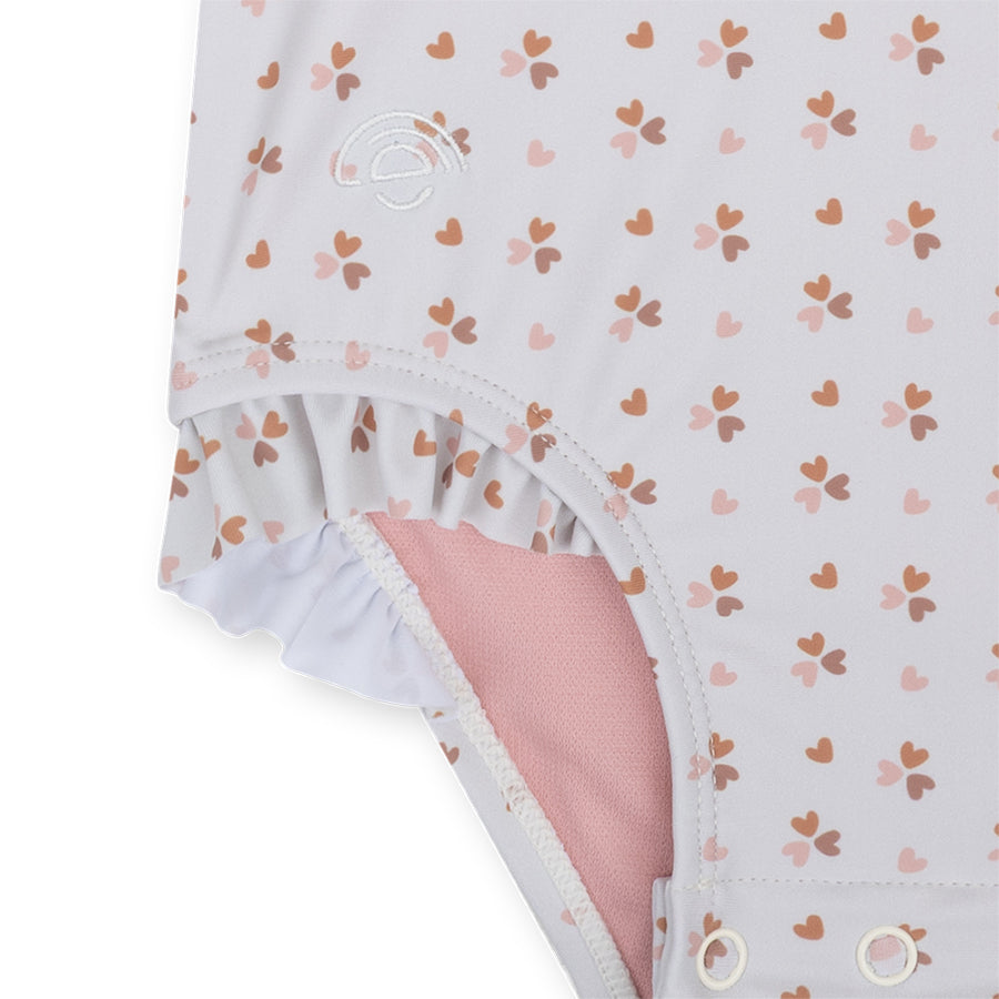 Close-up of the ruffles and part of the press stud fastening on the Old Pink Cozy Hearts swimsuit against a white background.